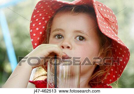 Stock Image - 3 year old girl in a big floppy red hat, drinking through a straw. Fotosearch