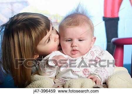 Stock Photo - 3 year old girl kissing 8 week old baby sister. Fotosearch