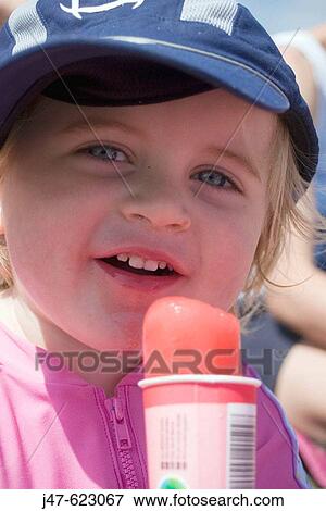 Stock Photo - 3 year old girl laughing into camera, holding an ice lolly on the beach. Fotosearch