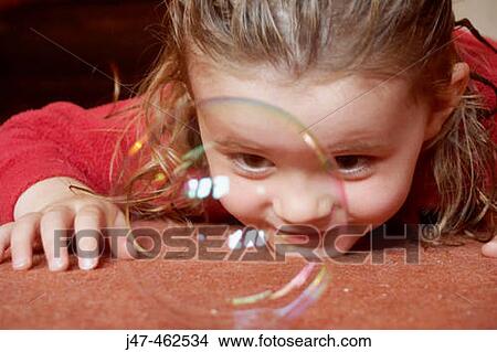 3 year old girl lying on the floor looking at a bubble right infront of her nose View Large Photo Image Picture - 3 year old girl lying on the floor looking at a bubble right infront of her nose. Fotosearch