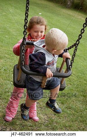 3 Year Old Girl Pushing And 18 Month Old Boy On A Swing Stock Image