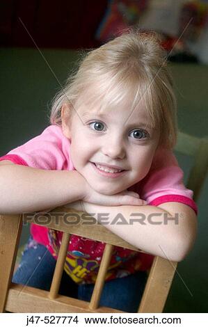 3 year old girl smiling into camera at nursery, leaning over the back of the chair onto her arms View Large Photo Image Picture - 3 year old girl smiling into camera at nursery, leaning over the back of the chair onto her arms. Fotosearch