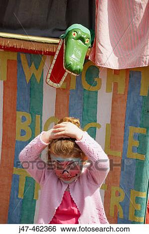 Stock Photograph - 3 year old girl standing in front of a Punch and Judy stall, with a crocodile snapping at her head.. Fotosearch