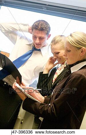 3 young business people standing in a group looking at papers, smiling View Large Photo Image Stock Photograph - 3 young business people standing in a group looking at papers, smiling. Fotosearch