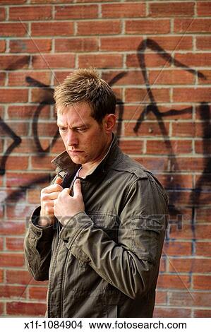 30 year old man alone wearing scruffy jacket standing against brick wall looking depressed sad alone lonely View Large Photo Image Picture - 30 year old man alone wearing scruffy jacket standing against brick wall looking depressed sad alone lonely. Fotosearch