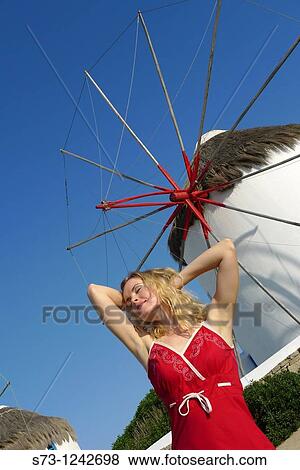 Stock Photo - 30 year old woman in front of windmill, Mykonos, Cyclades islands, Greece. Fotosearch