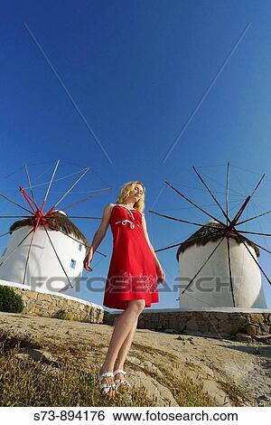Stock Photograph - 30 year old woman in front of windmill, Mykonos, Cyclades islands, Greece. Fotosearch
