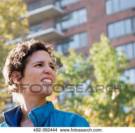 Picture - 33-year-old woman looking up in front of an apartment building in New York City. Fotosearch