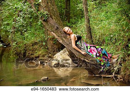 34 year old blond woman in a long flower print dress reclining on a tree in small creek looking at the camera View Large Photo Image Stock Image - 34 year old blond woman in a long flower print dress reclining on a tree in small creek looking at the camera. Fotosearch