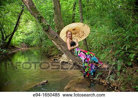 34 year old blond woman in a long flower print dress holding a parasol reclining on a tree in small creek looking at the camera View Large Photo Image Stock Photography - 34 year old blond woman in a long flower print dress holding a parasol reclining on a tree in small creek looking at the camera. Fotosearch