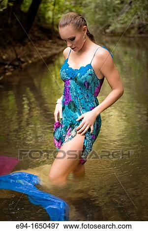 Stock Photo - 34 year old blond woman in a short flower print dress standing in a small creek looking down from the camera. Fotosearch