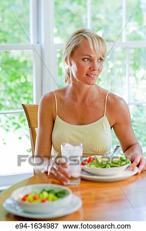 35 year old blond woman sitting at a kitchen table with a salad and a glass of water, selective focus View Large Photo Image Stock Photo - 35 year old blond woman sitting at a kitchen table with a salad and a glass of water, selective focus. Fotosearch