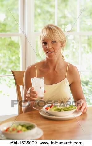 35 year old blond woman sitting at a kitchen table with a salad and a glass of water, selective focus View Large Photo Image Stock Photo - 35 year old blond woman sitting at a kitchen table with a salad and a glass of water, selective focus. Fotosearch