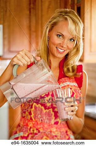 35 year old blond woman standing in a kitchen pouring a cold fruit drink from a blender into a glass View Large Photo Image Picture - 35 year old blond woman standing in a kitchen pouring a cold fruit drink from a blender into a glass. Fotosearch