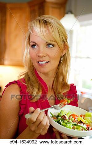 35 year old blond woman standing in a kitchen with a salad and holding a fork, looking away from the camera View Large Photo Image Stock Image - 35 year old blond woman standing in a kitchen with a salad and holding a fork, looking away from the camera. Fotosearch