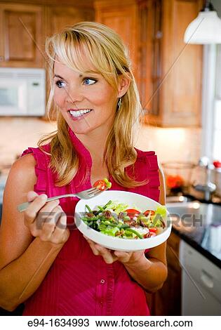 35 year old blond woman standing in a kitchen with a salad and holding a fork, looking away from the camera View Large Photo Image Stock Image - 35 year old blond woman standing in a kitchen with a salad and holding a fork, looking away from the camera. Fotosearch