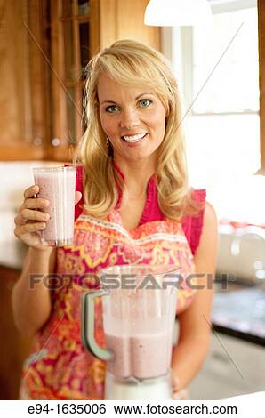 35 year old blond woman standing in a kitchen holding cold fruit drink, blender in foreground View Large Photo Image Stock Photograph - 35 year old blond woman standing in a kitchen holding cold fruit drink, blender in foreground. Fotosearch