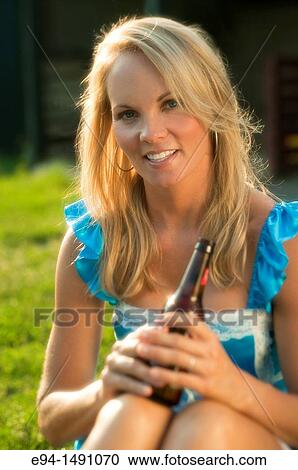 35 year old blond woman wearing a blue dress sitting on farm equipment smiling at camera holding a bottle of beer. View Large Photo Image Stock Image - 35 year old blond woman wearing a blue dress sitting on farm equipment smiling at camera holding a bottle of beer.. Fotosearch