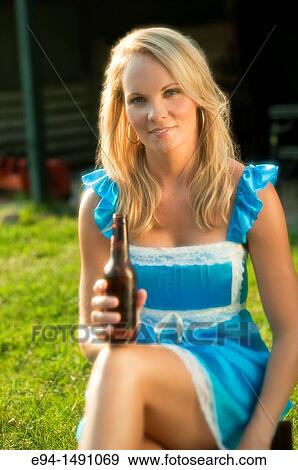 35 year old blond woman wearing a blue dress sitting on farm equipment smiling at camera holding a bottle of beer. View Large Photo Image Stock Photo - 35 year old blond woman wearing a blue dress sitting on farm equipment smiling at camera holding a bottle of beer.. Fotosearch