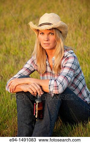 35 year old blond woman wearing jeans and a straw hat sitting on grass holding a bottle of beer. View Large Photo Image Stock Image - 35 year old blond woman wearing jeans and a straw hat sitting on grass holding a bottle of beer.. Fotosearch