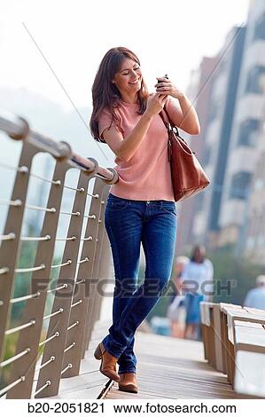 Stock Image - 35 year old woman with smartphone in town. Donostia. San Sebastian. Gipuzkoa. Basque Country, Spain.. Fotosearch
