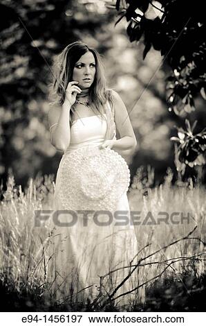 Stock Photo - 36 year old brunette woman in a white dress standing in an overgrown yard acting for the camera. Fotosearch