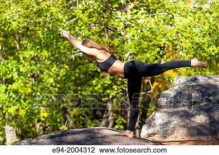 Stock Image - 37 year old brunette woman wearing fitness clothes doing a yoga pose in a forest setting.. Fotosearch