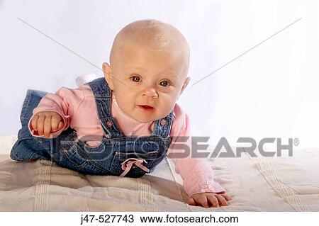 Stock Image - 4 month old baby girl, smiling off camera, lying on her tummy. Fotosearch