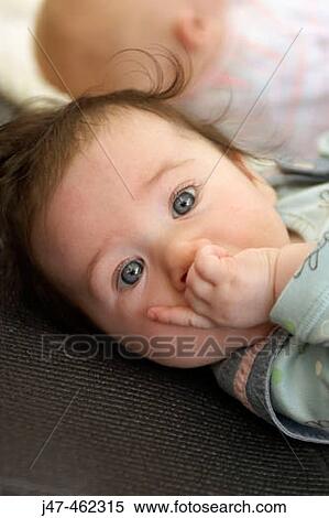 Stock Photography - 4 week old baby gazing into camera, fingers in her mouth. Fotosearch