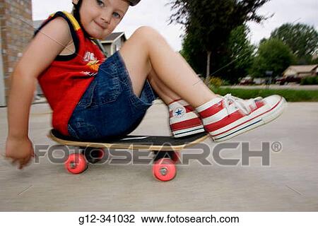 Stock Image - 4 year old boy riding skateboard while wearing red, white and blue shoes. Fotosearch
