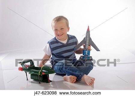 Stock Photo - 4 year old boy sitting on the floor in the studio with his aeroplanes, smiling off camera. Fotosearch
