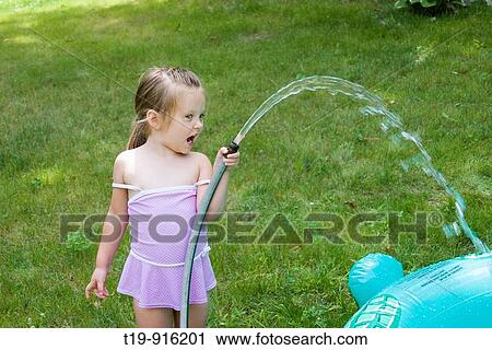 Stock Image - 4-year old girl filling her inflatable pool with water MR. Fotosearch