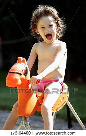 Stock Image - 4 year old girl sitting on a rocking horse.. Fotosearch