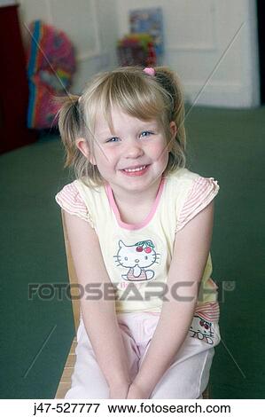 Stock Photo - 4 year old girl smiling into camera at nursery sitting on a small chair. Fotosearch
