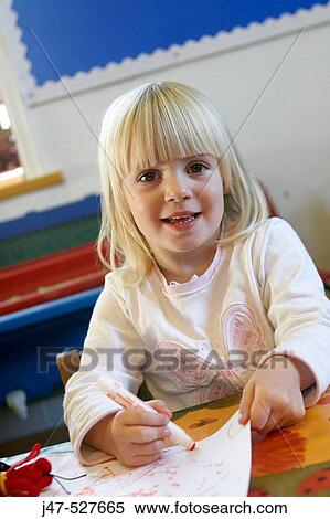 Stock Photography - 4 year old girl smiling into camera at nursery, drawing. Fotosearch