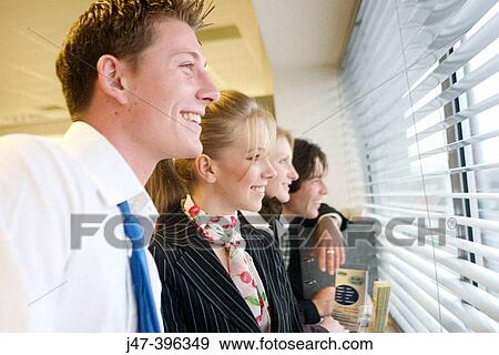 Stock Photo - 4 young business people standing in a line looking out of the window, selective focus. Fotosearch