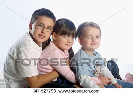 Stock Image - 5 year old girl sitting with her older and younger brothers, smiling into camera. Fotosearch