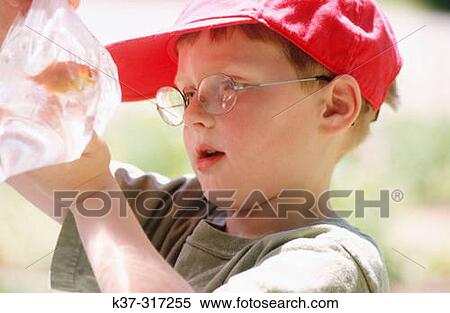 Stock Photography - 5 years old boy with reading glasses and baseball cap holding bag filled with water and goldfish. Fotosearch