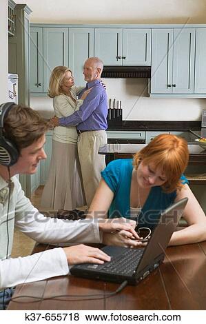 50-60 y/o couple dancing to music from stereo/radio in kitchen with teen/adult children sitting in dining room listening to music on laptop & ipod. View Large Photo Image Stock Photo - 50-60 y/o couple dancing to music from stereo/radio in kitchen with teen/adult children sitting in dining room listening to music on laptop & ipod.. Fotosearch