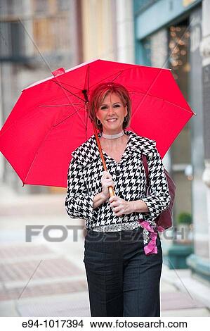 50 year old blonde woman walking on a city street carrying a red umbrella View Large Photo Image Picture - 50 year old blonde woman walking on a city street carrying a red umbrella. Fotosearch