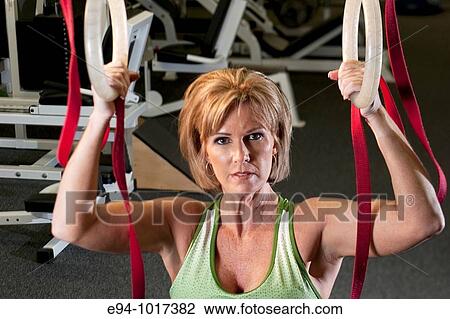 Stock Image - 50 year old woman in health club setting working out with equipment looking to the camera. Fotosearch