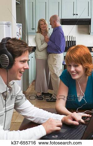50_60 y/o couple dancing to music from stereo/radio in kitchen with teen/adult children sitting in dining room listening to music on laptop & ipod. View Large Photo Image Stock Photograph - 50_60 y/o couple dancing to music from stereo/radio in kitchen with teen/adult children sitting in dining room listening to music on laptop & ipod.. Fotosearch