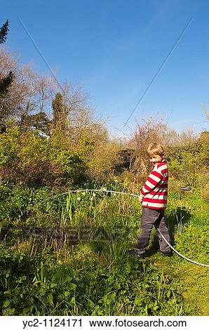 Stock Image - 6 year old boy filling a pond with a hose hosepipe in England, Great Britain, Uk. Fotosearch