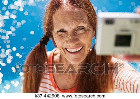 Stock Photo - 60-70 year old Caucasian woman, self portrait with digital camera. Fotosearch