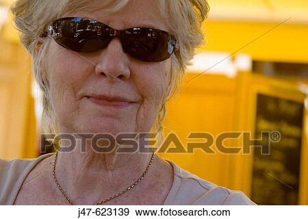 Stock Photo - 60_70 year od lady smiling into camera, wearing funky sunglasses, headshot. Fotosearch