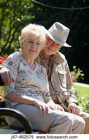 69, and 70 year old couple sitting on a park bench, hes got his arm round her, smiling into camera View Large Photo Image Stock Photography - 69, and 70 year old couple sitting on a park bench, hes got his arm round her, smiling into camera. Fotosearch