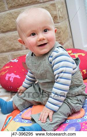 Stock Photography - 7 month old baby boy sitting on the floor smiling. Fotosearch
