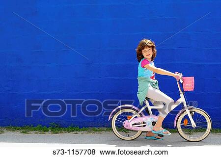 Stock Photo - 7 years old girl on bicycle front a blue wall in Caos de Meca, CBdiz, Andalucia, Spain. Fotosearch