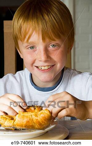 Stock Image - 8 yr old boy eating croissants. Fotosearch