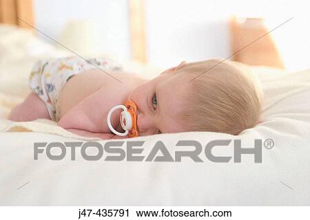 9 month old baby lying on his tummy on the bed with a dummy in his mouth View Large Photo Image Stock Image - 9 month old baby lying on his tummy on the bed with a dummy in his mouth. Fotosearch